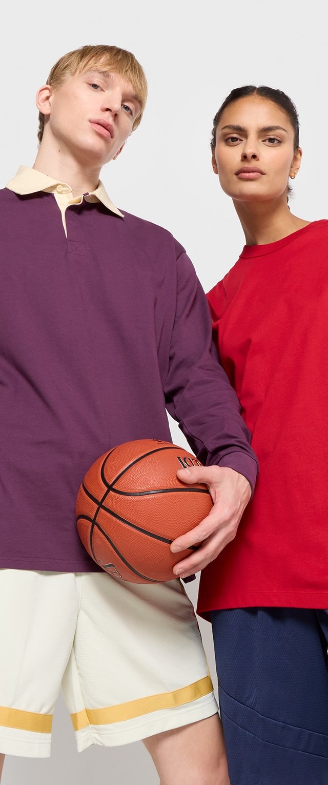 Dos personas sostienen un baloncesto. Uno viste una camiseta de manga larga morada con un cuello claro y pantalones cortos blancos con rayas amarillas. El otro lleva una camiseta roja y pantalones cortos azul marino.