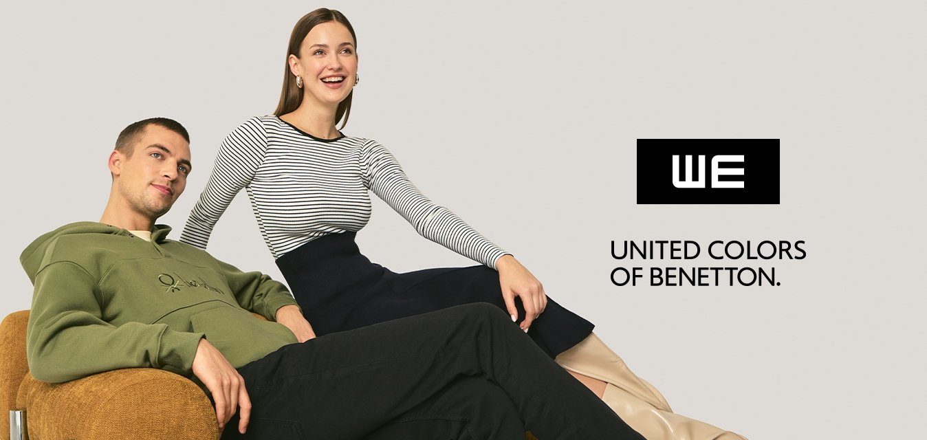 Zelená mikina s kapucí, pruhovaný top, černá sukně a béžové boty. Modelka sedí na hnědé texturované pohovce s chromovanými prvky na neutrálním pozadí.