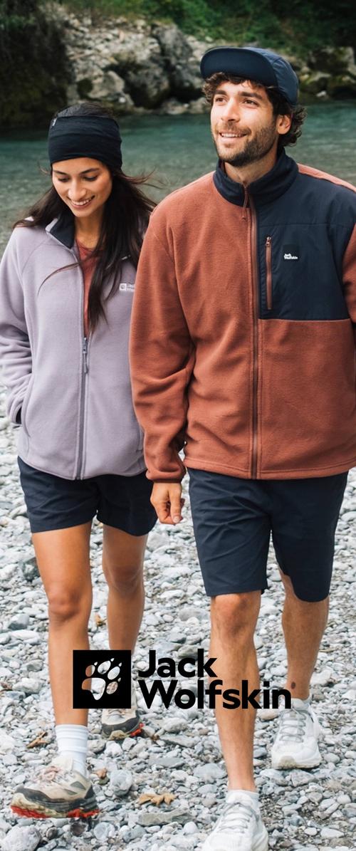 Dos personas caminan por un sendero rocoso, vistiendo chaquetas Jack Wolfskin: una de forro polar gris claro y la otra de color marrón rojizo con un acento negro.