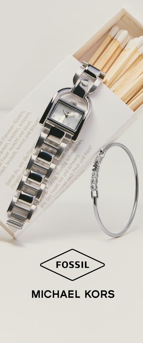Zilveren polshorloge met zwarte schakels geplaatst op een luciferdoosje met witgekleurde lucifers, naast een zilveren armband met heldere stenen. Fossil en Michael Kors logo's.