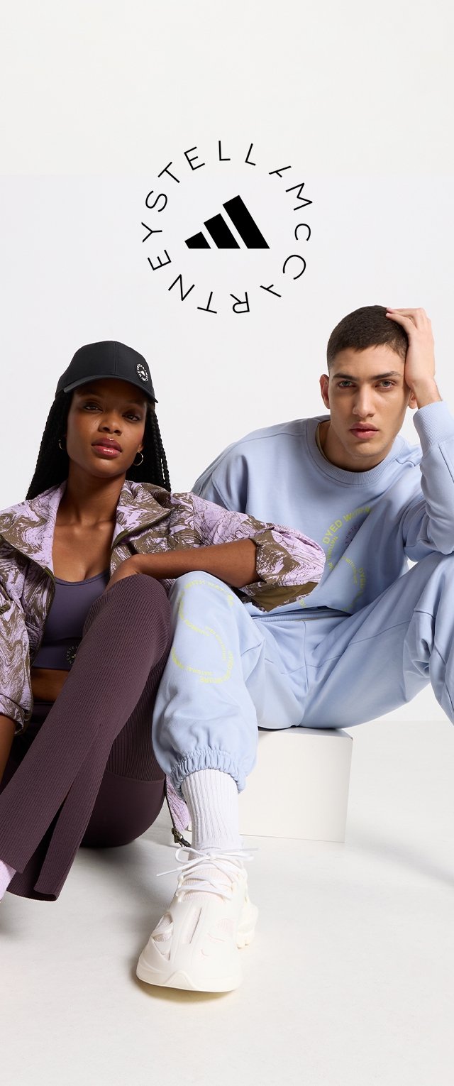 Sportsbeklædning bestående af en jakke med lavendel mønster, en grå sweatshirt og lilla ribbede leggings. Inkluderer en sort kasket og hvide sneakers.