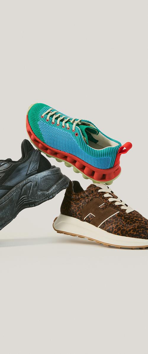 Tres zapatillas diferentes apiladas: suela negra gruesa, azul y verde con suela roja, y marrón con estampado de leopardo, suela y cordones blancos.
