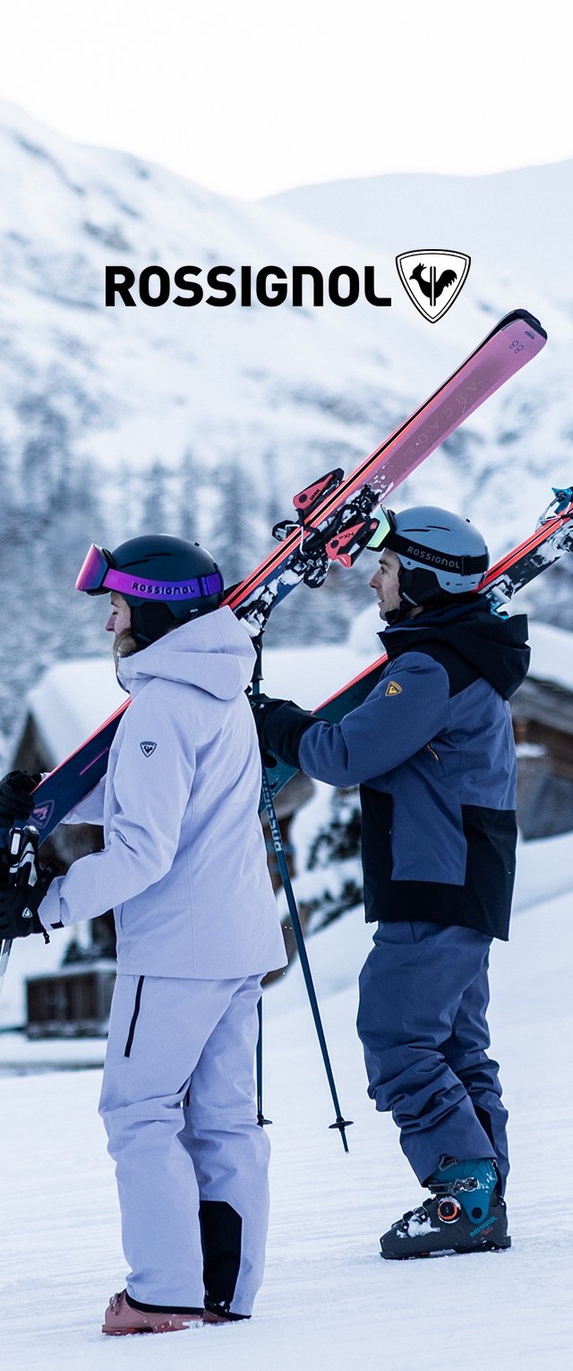 Dos esquiadores con cascos y ropa de invierno llevan esquís en un terreno montañoso nevado, con el logo y el nombre de la marca Rossignol sobre ellos.