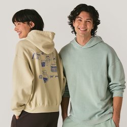 Usmívající se muž a žena oblékající pastelové mikiny a volné kalhoty, stojící vedle sebe na jednobarevném světlém pozadí.