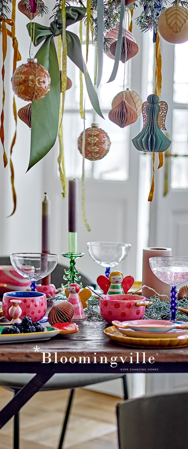 Farbige Tischdekoration mit gemusterten Keramiktellern, transparentem Glasgeschirr, Kerzen und hängenden Ornamenten in verschiedenen Formen und Texturen.