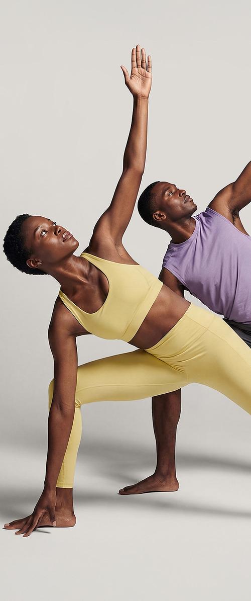 Dos personas con ropa deportiva realizando una postura de yoga de estiramiento lateral, con un brazo levantado y el otro tocando el suelo.