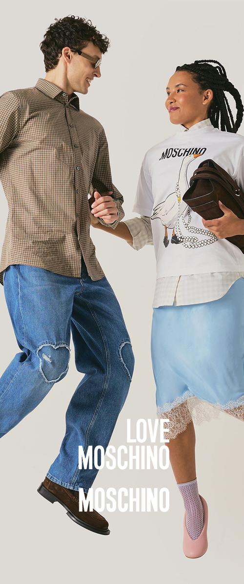 A man and woman smiling and holding hands mid-jump, wearing casual Moschino clothing with the brand name visible on the woman's shirt.