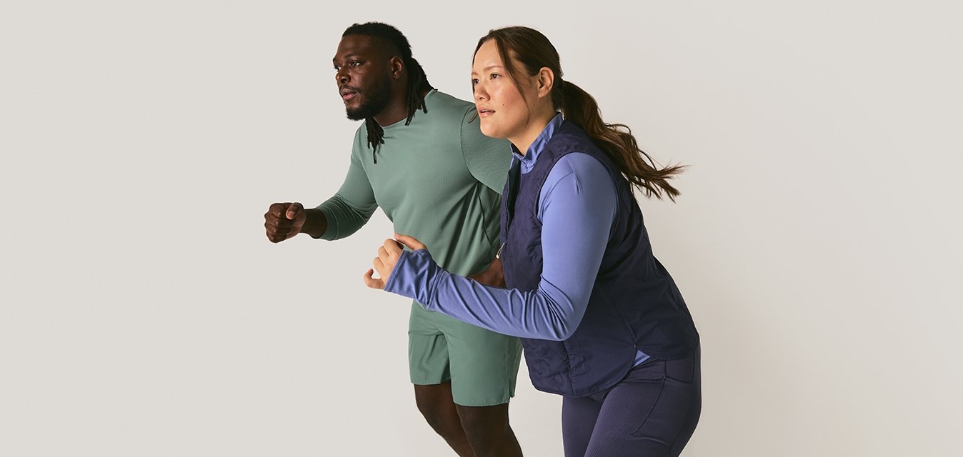 Muž a žena v sportovním oblečení se postavili, jako by byli připraveni ke startu, na jednobarevném světlem pozadí.