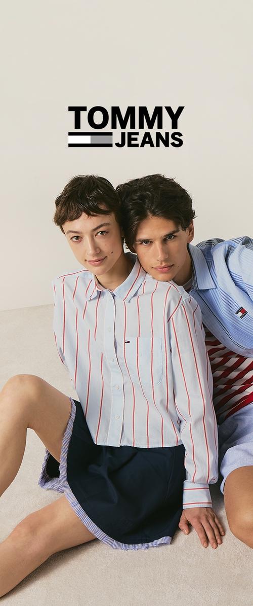 Deux jeunes mannequins sont assis l’un près de l’autre, portant des chemises rayées Tommy Jeans, sous le logo Tommy Jeans sur un fond clair uni.