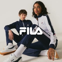Dvě osoby oblečené ve tmavě modrých a bílých teplákových soupravách značky FILA a bílých teniskách sedí na zemi před jednobarevným světlým pozadím.