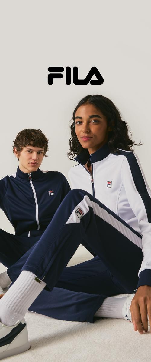 Deux mannequins assis portent des survêtements Fila bleu marine et blanc avec les logos Fila, sur un fond uni avec le logo Fila au-dessus d'eux.