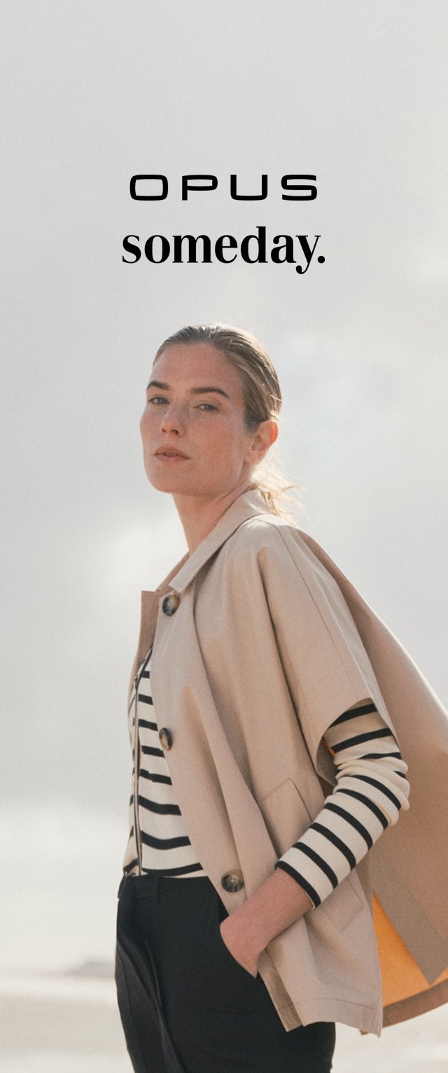 Lichtbeige buitenkleding met grote knopen over een zwart-wit gestreept shirt; model staand tegen een zachte achtergrond.