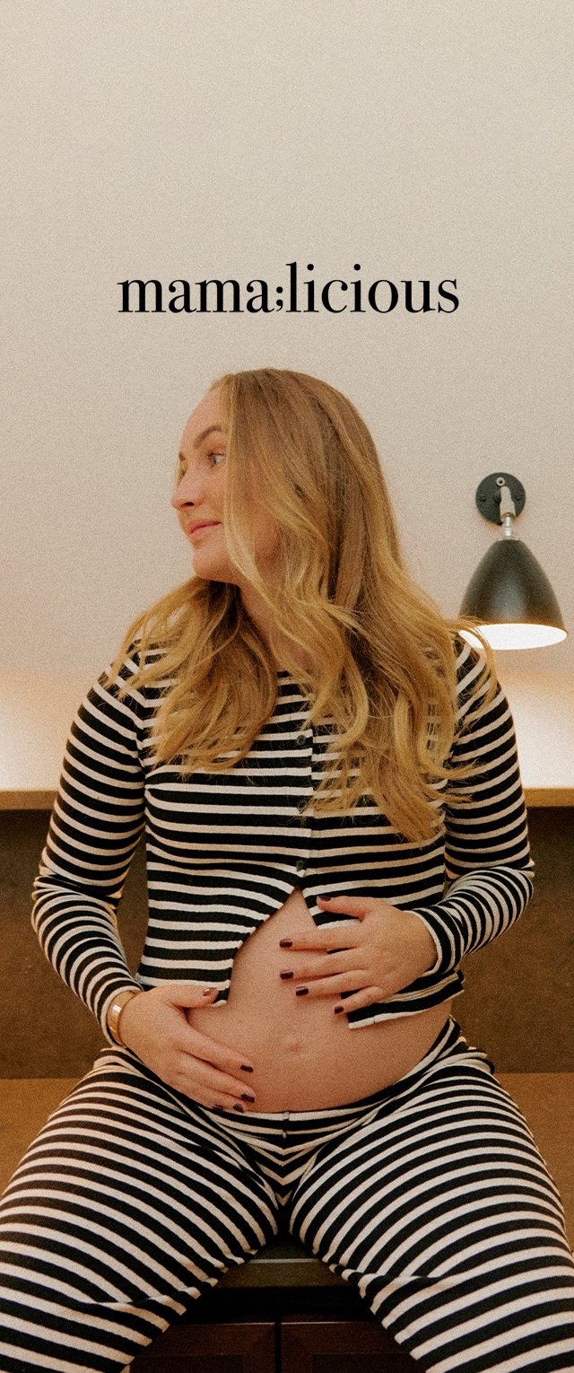 Schwarz-weiße gestreifte Umstandspyjamas mit einem taillierten Oberteil und lockeren Hosen, getragen von einem Modell, das ihren Bauch umarmt, vor einem neutralen Hintergrund.