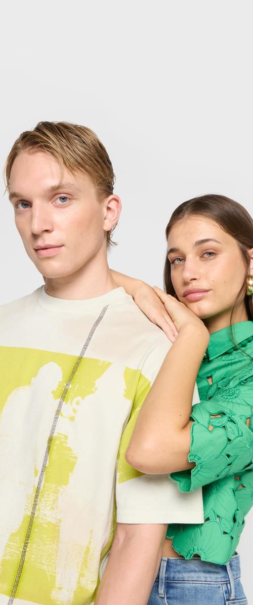 Dva modely oblečení v každodenním stylu: světle zbarvené tričko s grafickým motivem na zeleném pozadí a texturovaný zelený top s výstřihovými detaily.