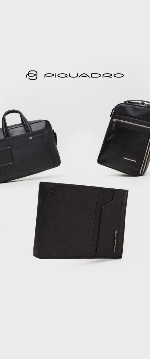 Portefeuille en cuir noir avec surface texturée, fente pour cartes à l'avant et logo en relief. Deux sacs noirs visibles à l'arrière-plan.