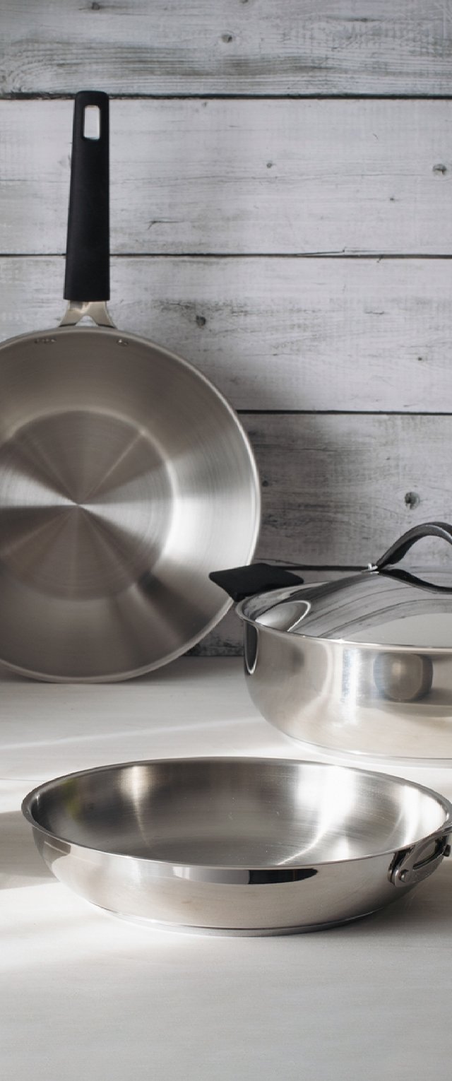 Tres utensilios de cocina de acero inoxidable: una sartén, una cacerola con tapa y una sartén grande con mango negro.